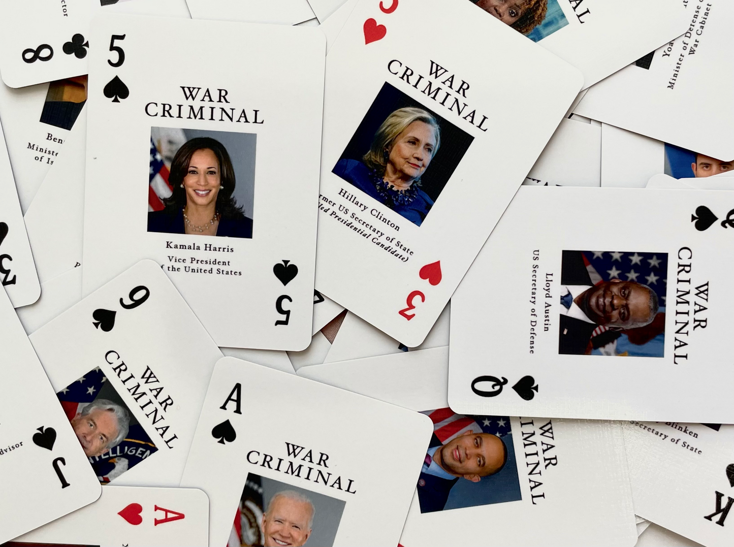 A photo of playing cards scattered face up: some faces include Kamala Harris, the 5 of Spades, Joe Biden, the Ace of Spades, Hillary Clinton. The 3 of Hearts and Lloyd Austin, the Queen of Spades.